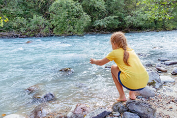 Rear view adorable little child girl playing and having fun near mountain river on warm and sunny summer day. (Holiday, rest, happy childhood concept), copy space