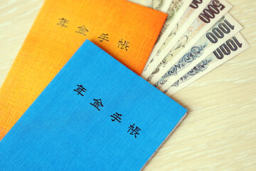 Japanese pension insurance booklets on table with yen money bills. Blue and orange books for japan...