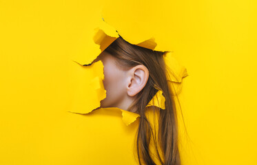 Female ear and long hair close-up. Copy space. Torn paper, yellow background. The concept of...