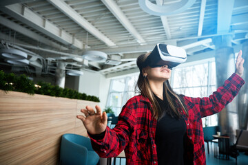Young concentrated female IT worker using VR glasses in hall of coworking office