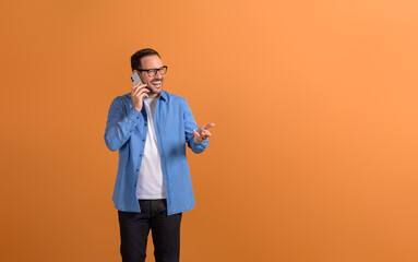 Cheerful male professional in eyeglasses discussing strategies over smart phone on orange background
