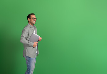 Side view of determined businessman holding laptop and thinking business ideas on green background