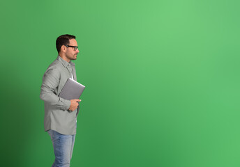 Side view of male entrepreneur holding laptop and thinking ideas while standing on green background