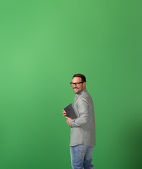Side view of successful businessman with laptop smiling at camera over shoulder on green background