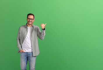 Portrait of salesman aiming thumbs at copy space and demonstrating new product on green background