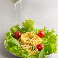 Pasta with vegetables is seasoned with salt on a gray background. Too much salt in food is unhealthy. It is necessary to salt food in moderation