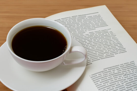 book with mug. an open book with a white mug of coffee lies on a wooden table, top view, close-up, reading concept