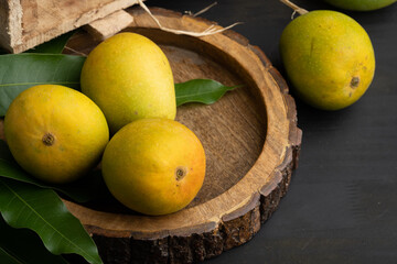 Mango heap in wood basket carrying by a orchard farmer with green leaf background.