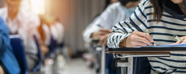 Exam at school with student's taking educational admission test in class, thinking hard, writing answer in university classroom, education and world literacy day concept