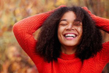 Young happy overjoyed curly african american woman with eyes closed and laughing in autumn forest