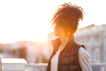Rear view of young woman standing at rooftop in morning sunlight
