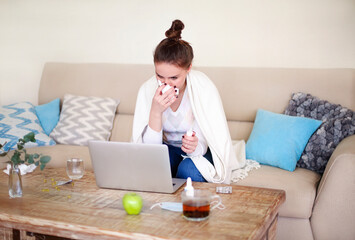 Sick woman sitting on sofa near the computer trying to work at home