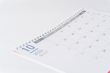 A spiral bound paper calendar. October page of 2024 calendar displayed on white background, side view and selective focus shot. 