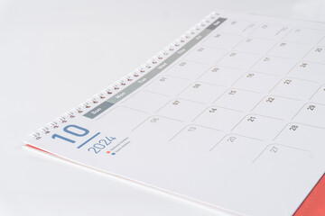 A spiral bound paper calendar. October page of 2024 calendar displayed on white background, side view and selective focus shot. 
