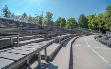 Amfiteatr, stadion, ławki ułożone w okrąg. Letni dzień, w południe, w parku miejskim, na widowni muszli koncertowej pod słonecznym, błękitnym niebem.