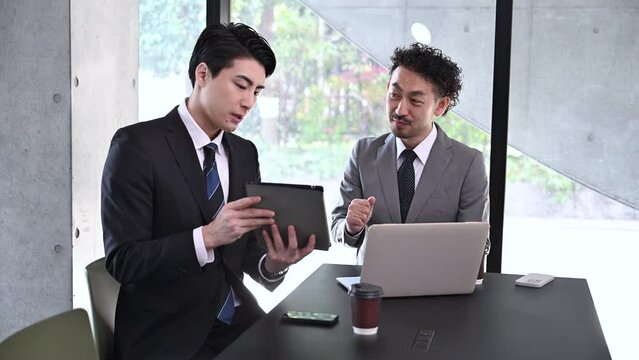 Two men in a meeting using a tablet by the window Video of an image of a boss listening to a sales person or subordinate making a proposal for a project or job.