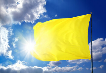 Conceptual image of waving blank yellow flag over sunny blue sky