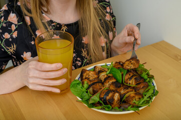 Dziewczyna je obiad przy stole, mięsne szaszłyki z grilla z sałatą, popija pomarańczowym sokiem