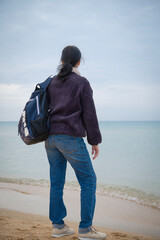 Solo backpacking to the sea. A woman with a backpack stands on the shore and looks into the distance. A woman with a backpack stands on the shore and looks into the distance.