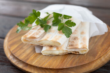 A pita bread roll with cheese is served on a wooden board
