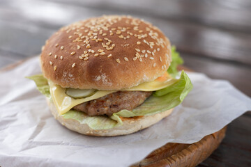 Cheeseburger sandwich loaded with sliced tomatoes, pickles, and lettuce on top of a sesame seed bun