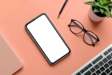 Top view of smartphone with a blank screen placed on peach fuzz background, surrounded by eyeglasses, a laptop, and small plant.