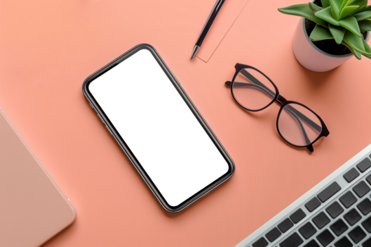 Top view of smartphone with a blank screen placed on peach fuzz background, surrounded by eyeglasses, a laptop, and small plant.