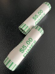 Two complete rolls of dimes in green and white wrappers that are sitting on a black table top that offers great contrast.
