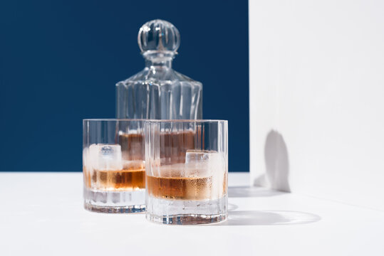 Dos vasos de whisky escocés con hielo y decantador sobre fondo azul