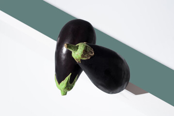 Dos berenjenas frescas sobre un soporte blanco y fondo verde. Vista superior
