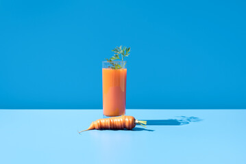 Jugo de zanahoria adornado con hojas verdes en un vaso transparente sobre fondo azul