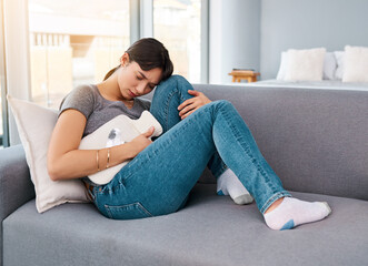 Stomach pain, stress or girl on sofa with hot water bottle for pms gas, constipation or period crisis at home. Tummy, digestion or anxiety in living room with heating pad for endometriosis or pcos © peopleimages.com