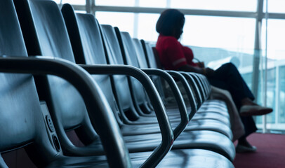 Silhouette of a woman sitting in the waiting area at an international airport terminal in Paris. The woman observes the moving planes through the large glass windows. Selective focus