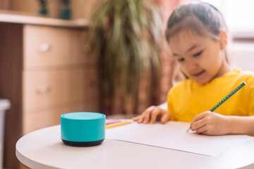 Child draws at the table and talks to a blue smart speaker.