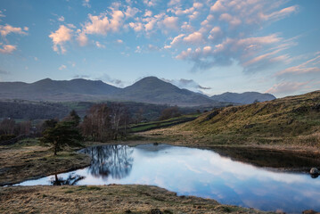 Stunning sunset landscape image of Kelly Hall Tarn in Lake District with Old Man of Coniston in background