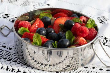 CLOSE UP SUMMER FRUITS WITH MINT LEAVES IN TIFFIN TIN ON VINTAGE WHITE CLOTH