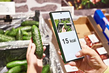 Checking calories on cucumber vegetable in store with smartphone