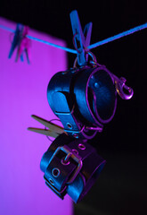 bdsm leather handcuffs hanging on a clothesline in neon light on a black background