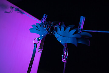 bdsm leather shoulder straps in the shape of wings hanging on a clothesline in neon light on a...