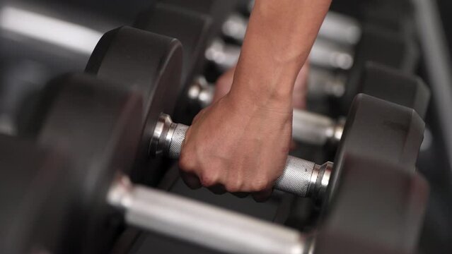 Close-up of hands gripping dumbbell on weight rack in gym, workout gear