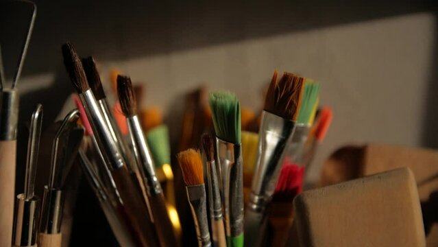 A close-up shot of paint brushes and modeling clay tools in ceramic vases.