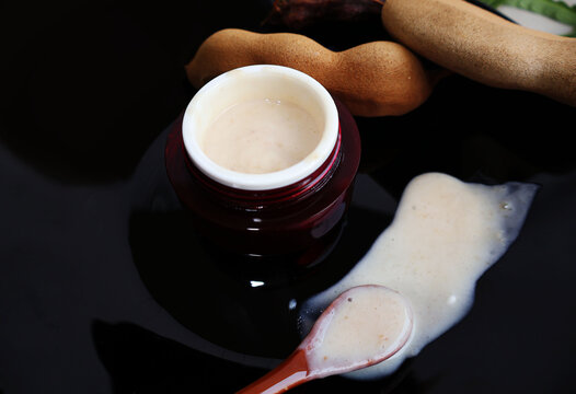 Skin cream containing ingredients from ripe tamarind pulp in a red jar. Scoop out the cream and pour it on the black tile floor. Place the ripe fruit next.