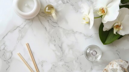 Top-view shot of a white marble countertop with a clear glass bottle of essential oil, a single white orchid, and a minimalist diffuser