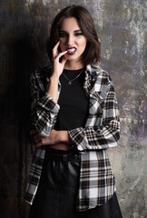 Portrait of naughty grunge (rock) girl. Cool informal model, dressed in checkered shirt and leather...