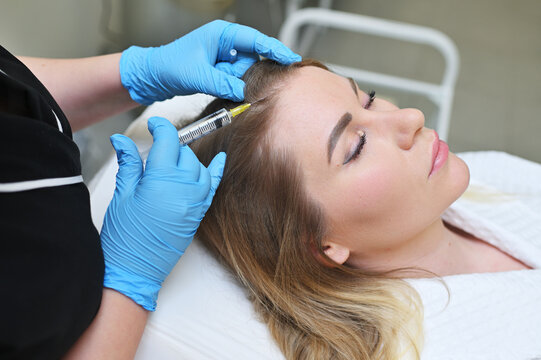 dermatologist cosmetologist performs a mesotherapy procedure and injects an injection into the scalp of a young woman patient.