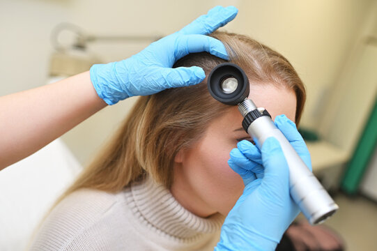 dermatologist trichologist examines the hair structure of a young woman's patient using an optical dermatoscope device.