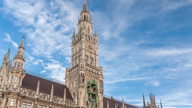 Marienplazt Old Town Square with Town Hall Clock Tower Glockenspiel timelapse. Neues Rathaus, the New Town Hall. Munich skyline, downtown cityscape with clouds on a blue sky. Bavaria, Germany