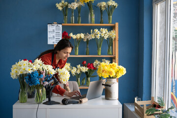 Female florist owner of a small business flower shop. Florist uses laptop while working in her flower shop