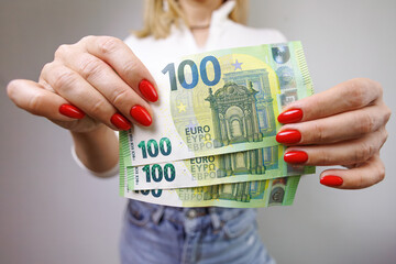 A close-up of a euro bill with a denomination of one hundred which is held by a woman's hands. A girl in jeans with a euro banknote in her hands. - obrazy, fototapety, plakaty
