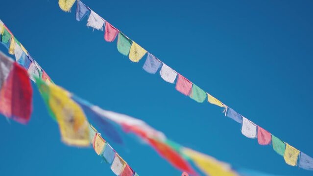 Closeup slow motion shot of Buddhist prayer flags against the clear blue sky at Sani Monastery near Padum in Zanskar Valley, Ladakh, India. Prayer flags waving in front of sky, Religious background.	